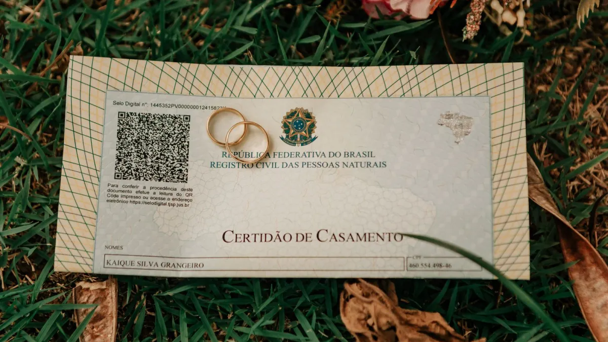 Certidão de casamento brasileira com alianças sobre a grama